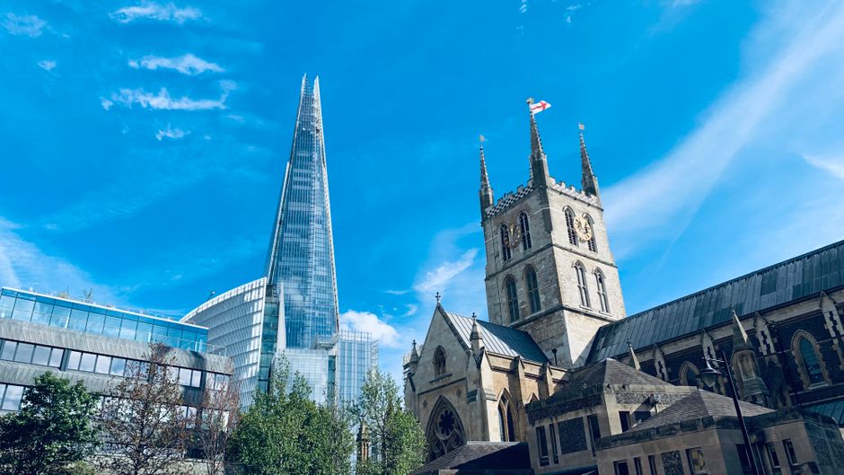 A busy outdoor scene at Borough Market with a large crowd of people gathered under the market's signage. The market entrance features modern architectural elements with a mix of metal and glass struct